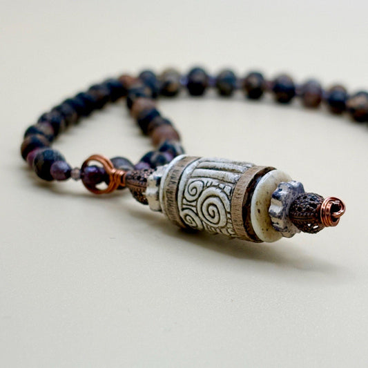 Necklace with dark beads and a decorative clasp on a light background