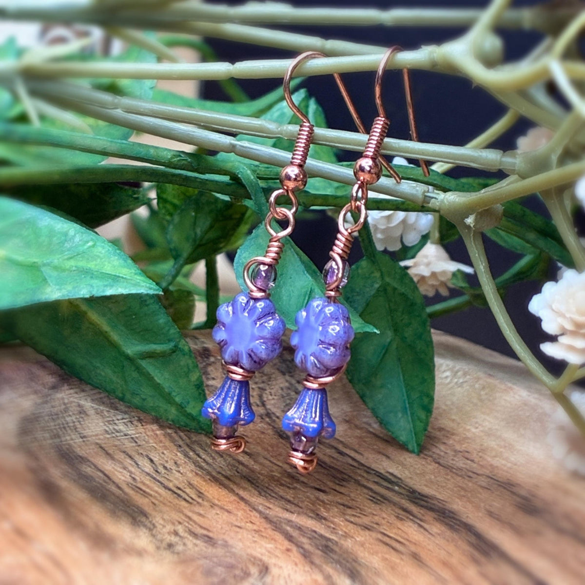 copper wire wrapped earrings with purple flowers hanging from a branch