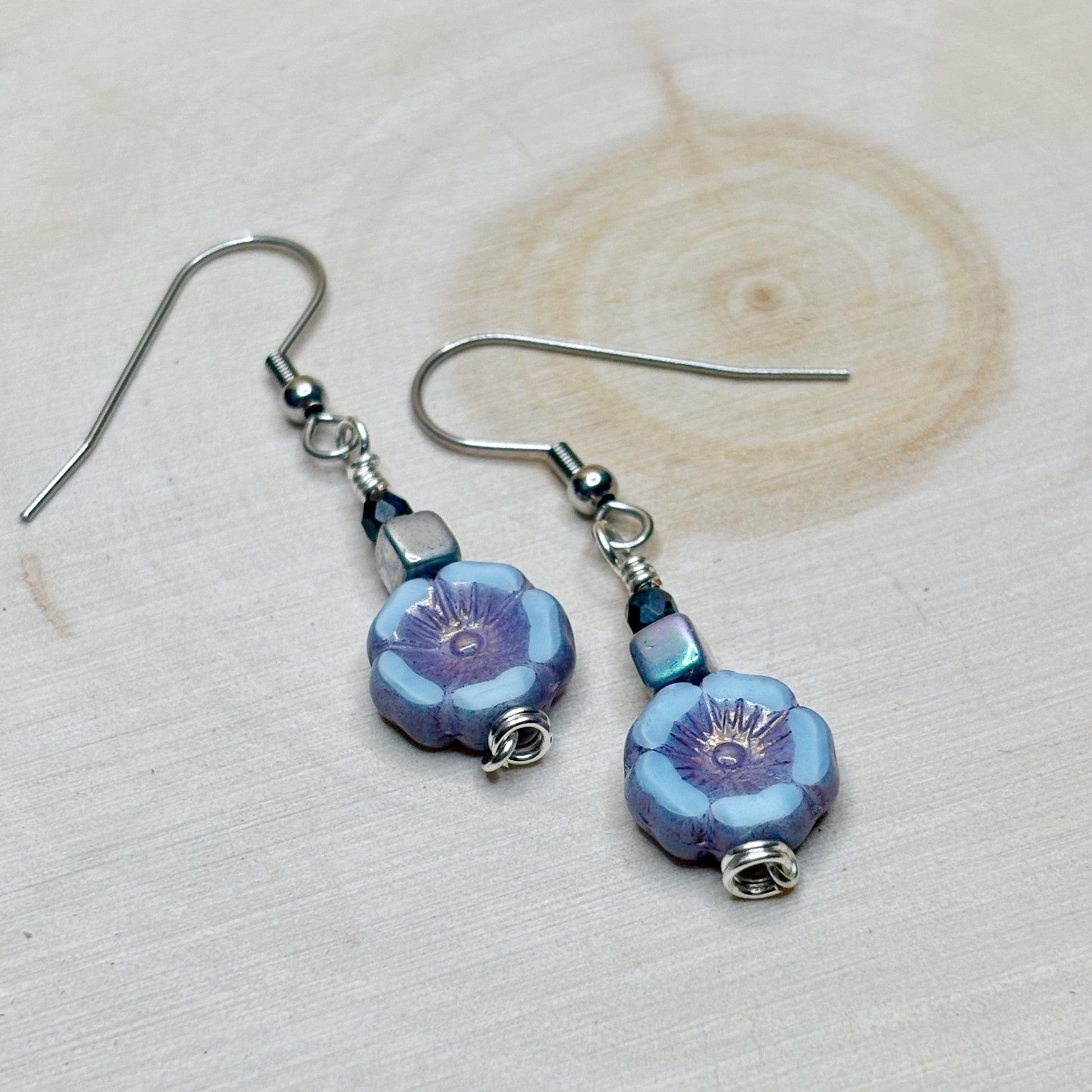 Pair of floral earrings with blue and purple flowers on a light wooden background