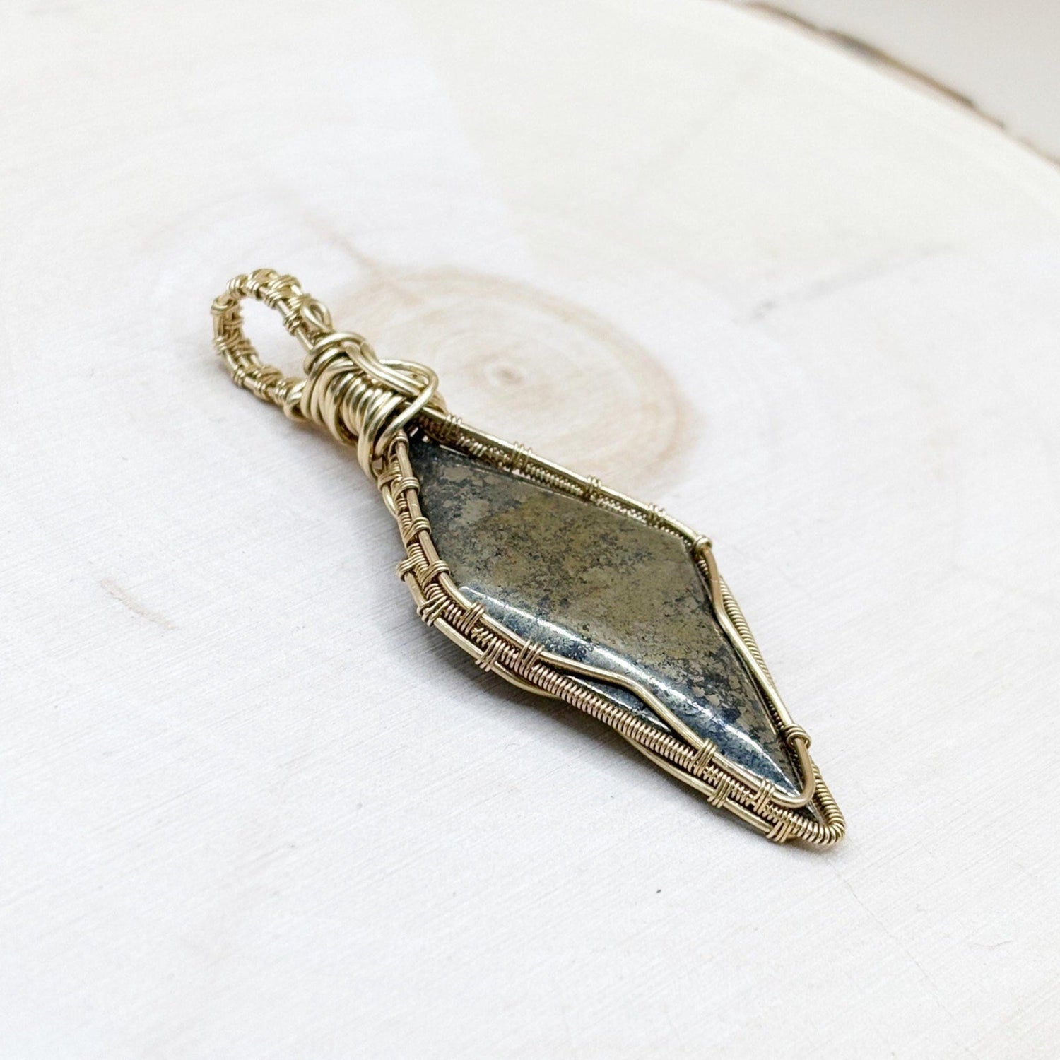 Decorative stone pendant with gold wire wrapping on a white wood background