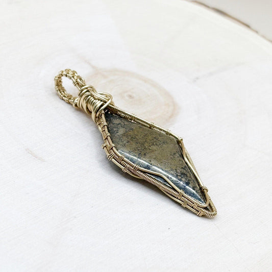Decorative stone pendant with gold wire wrapping on a white wood background-p