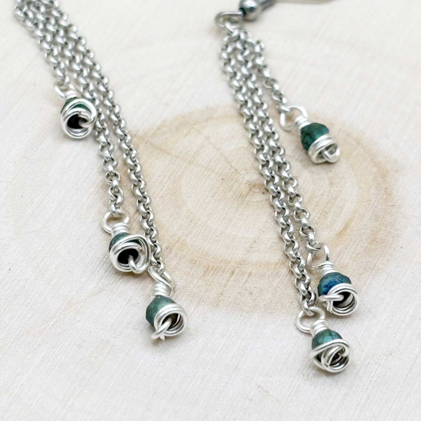 Silver earrings with green beads on a textured white surface