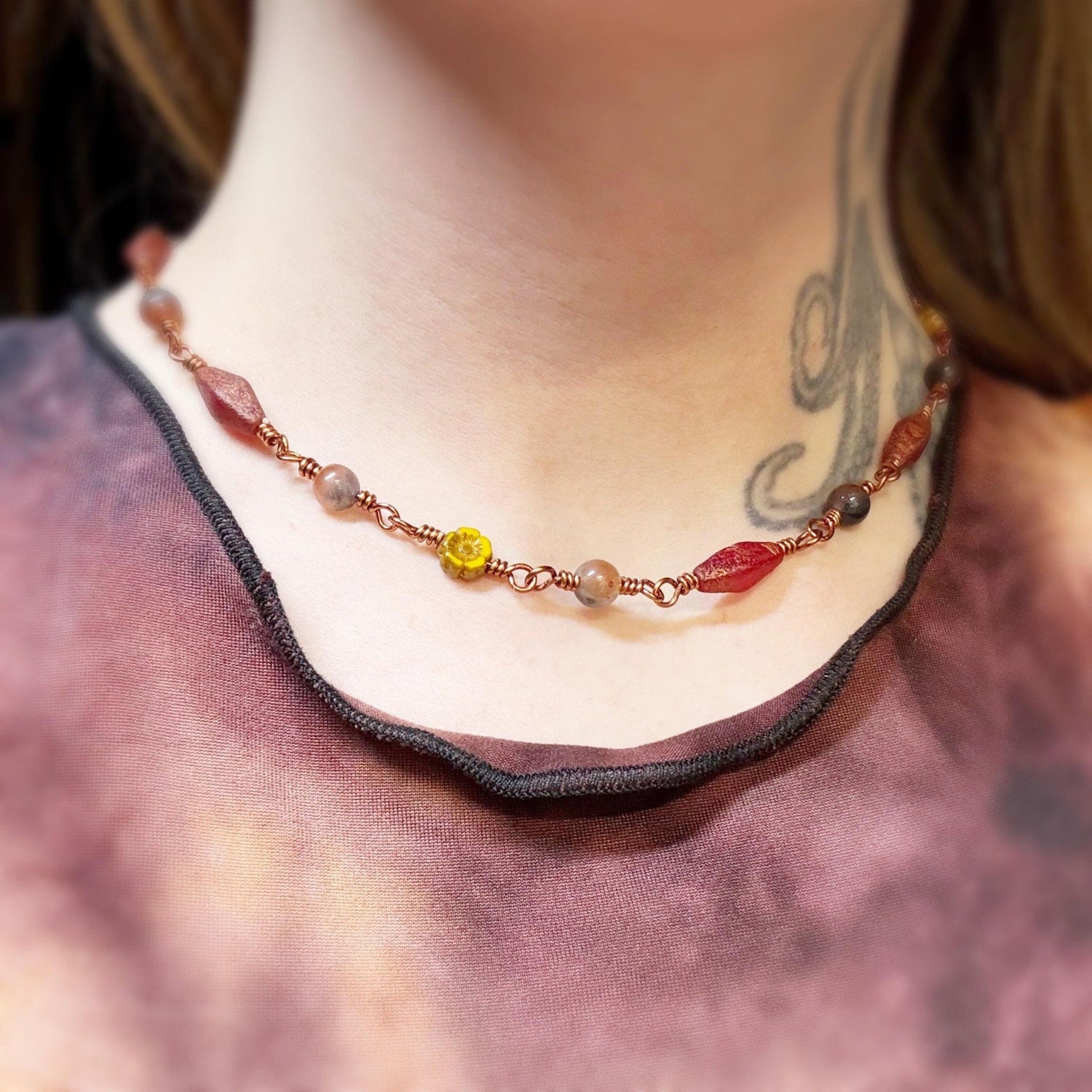 Necklace with red and yellow beads worn by a person with a tattoo on their neck.