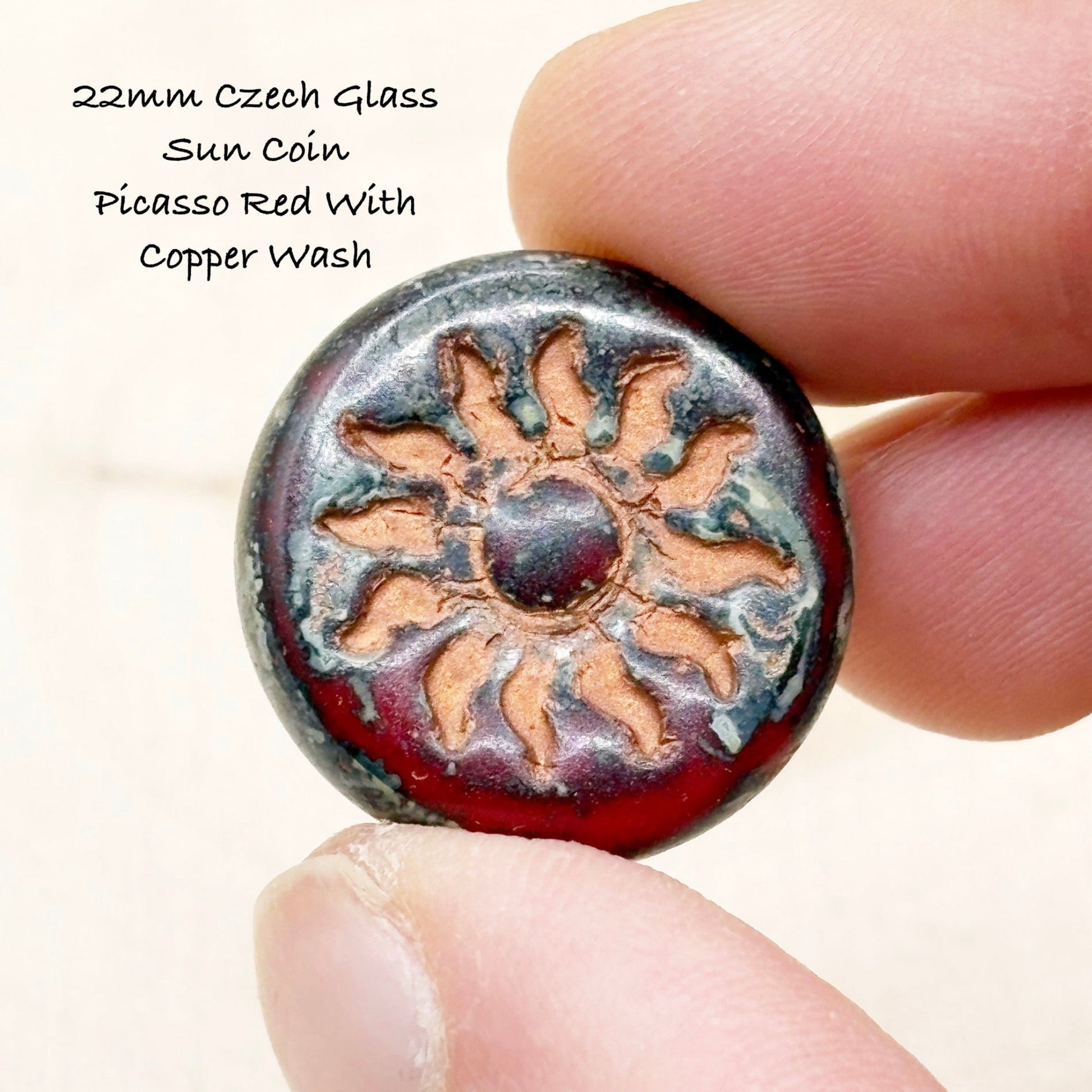 22mm Czech Glass Sun Coin Picasso Red With Copper Wash held between fingers