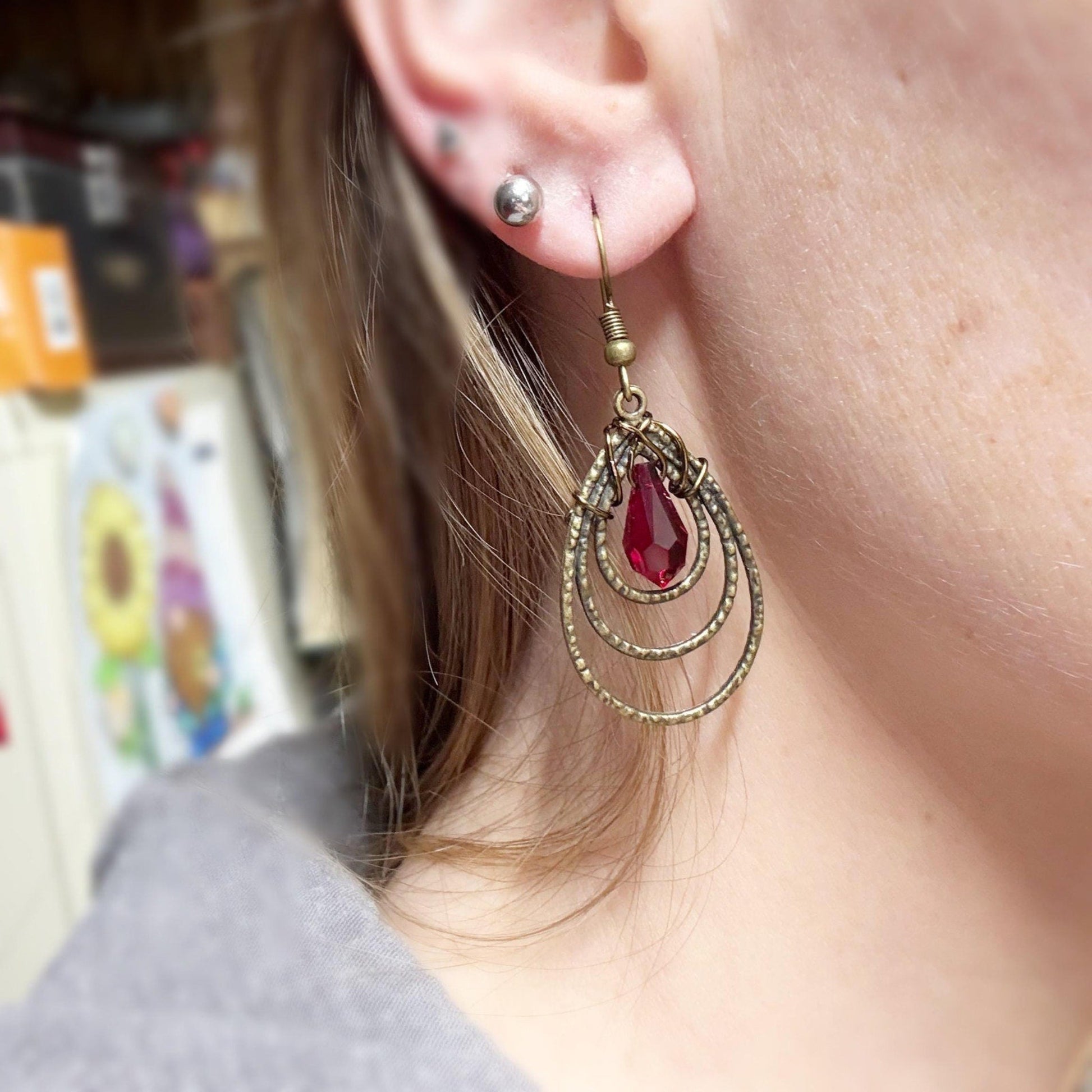 Close-up of an ear wearing a gold and red earring with a blurred background.