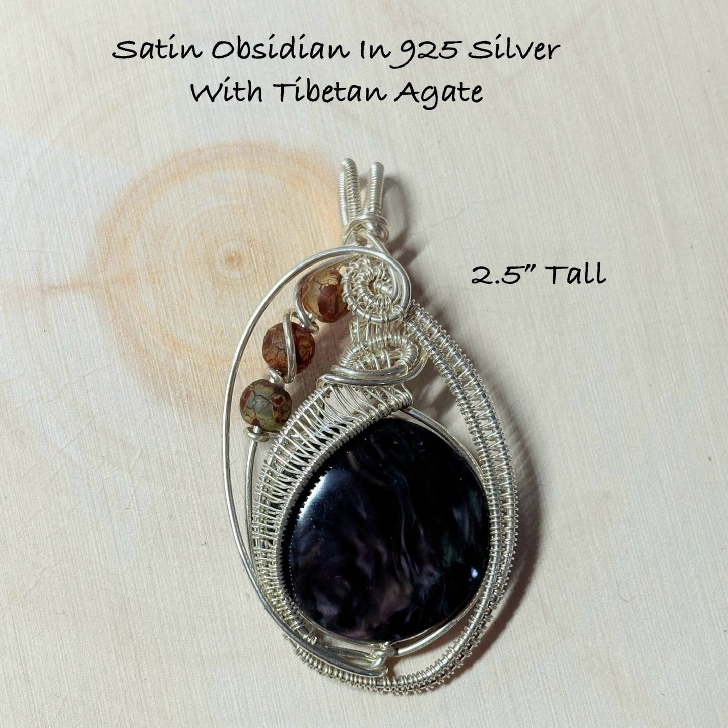 Silver pendant with obsidian stone and Tibetan agate on a wooden surface