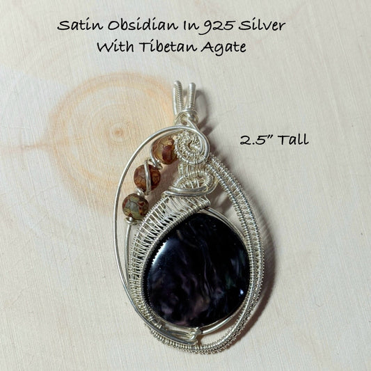 Silver pendant with obsidian stone and Tibetan agate on a wooden surface