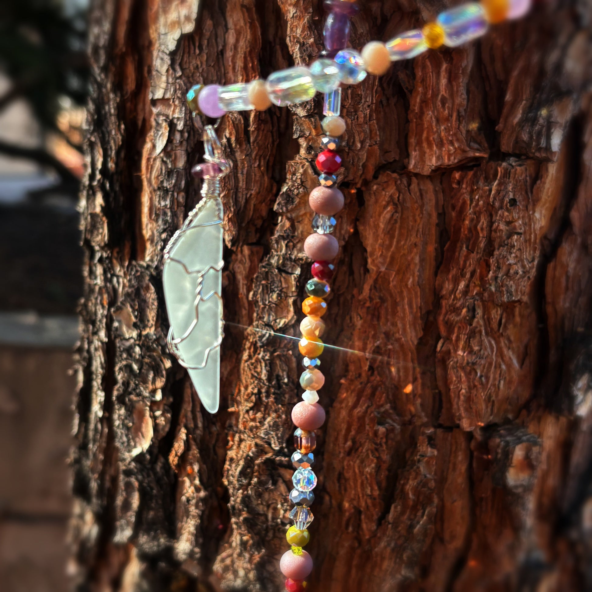 Colorful beaded sun catcher with a sea glass pendant on a textured wooden surface