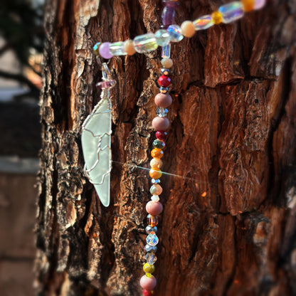 Colorful beaded sun catcher with a sea glass pendant on a textured wooden surface