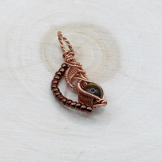 Copper wire-wrapped pendant with a central stone on a textured wood white background