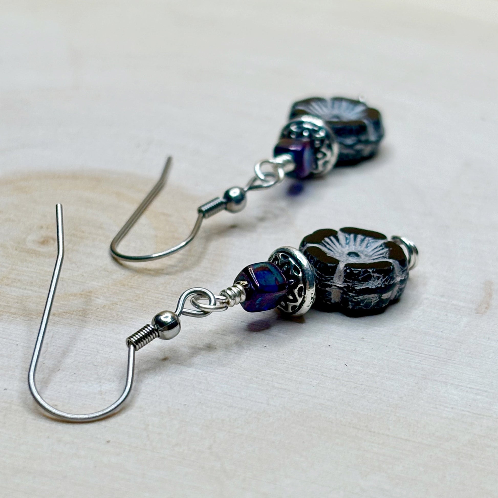 Pair of silver earrings with purple and black beads on a light background