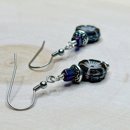 Pair of silver earrings with purple and black beads on a light background