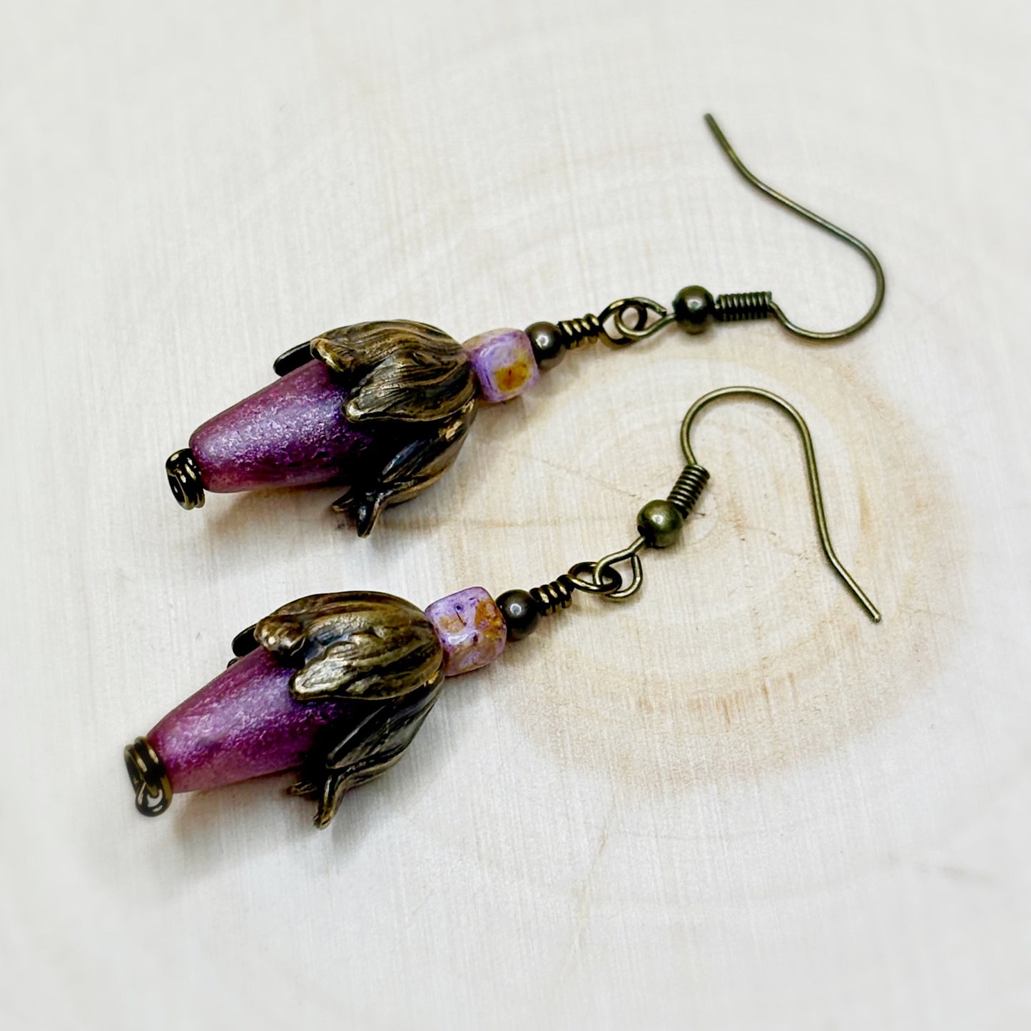 Pair of earrings with purple beads and bronze accents on a light background