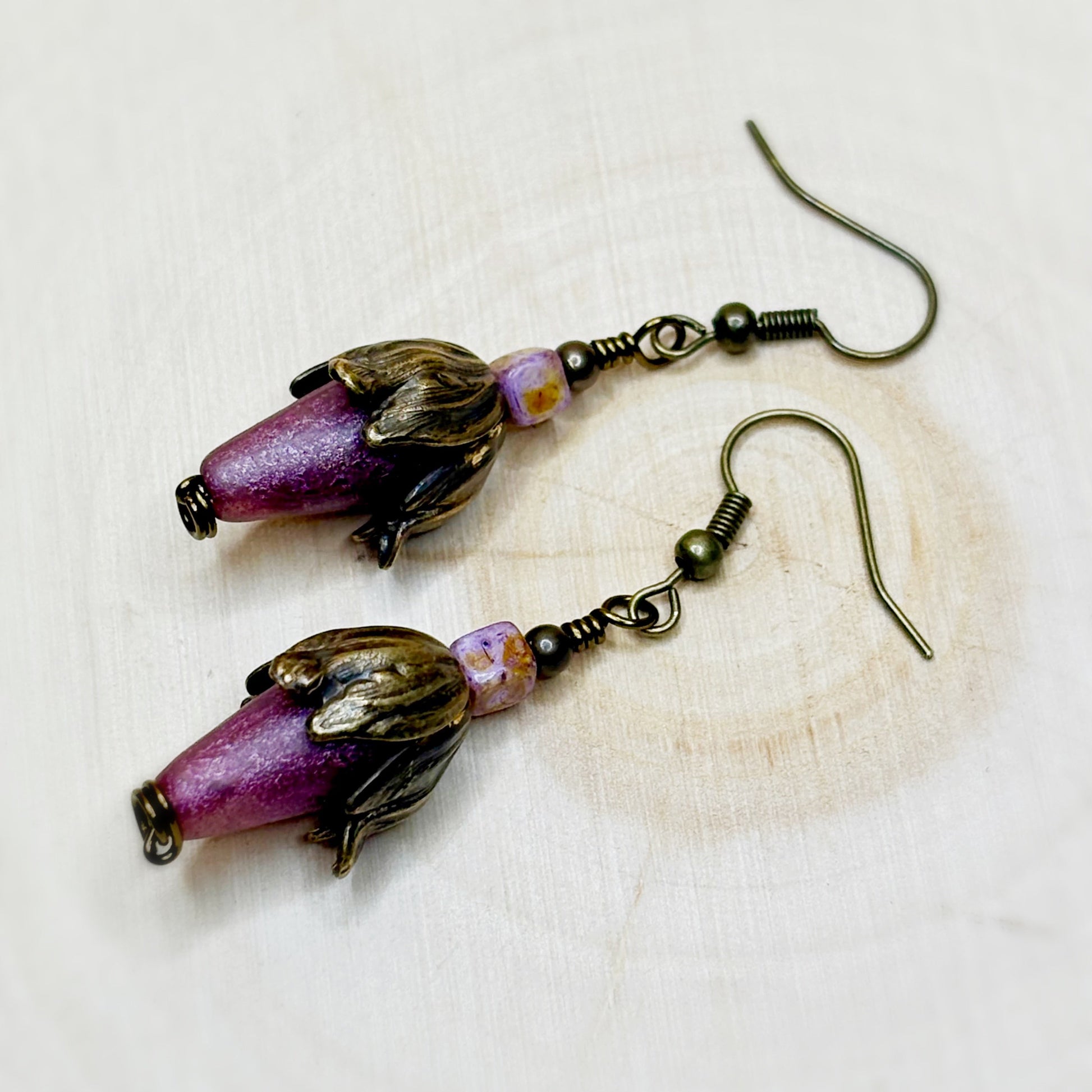 Pair of earrings with purple beads and bronze accents on a light background