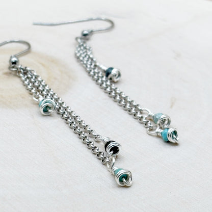 Silver chain earrings with blue and black accents on a light background