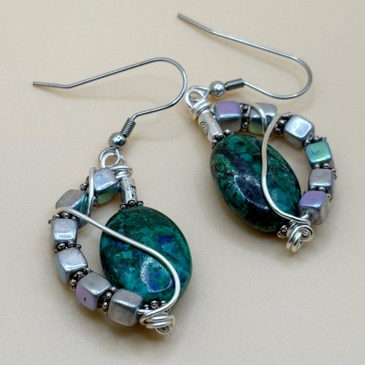 Pair of earrings with green stone and silver wire wrapping on a beige background