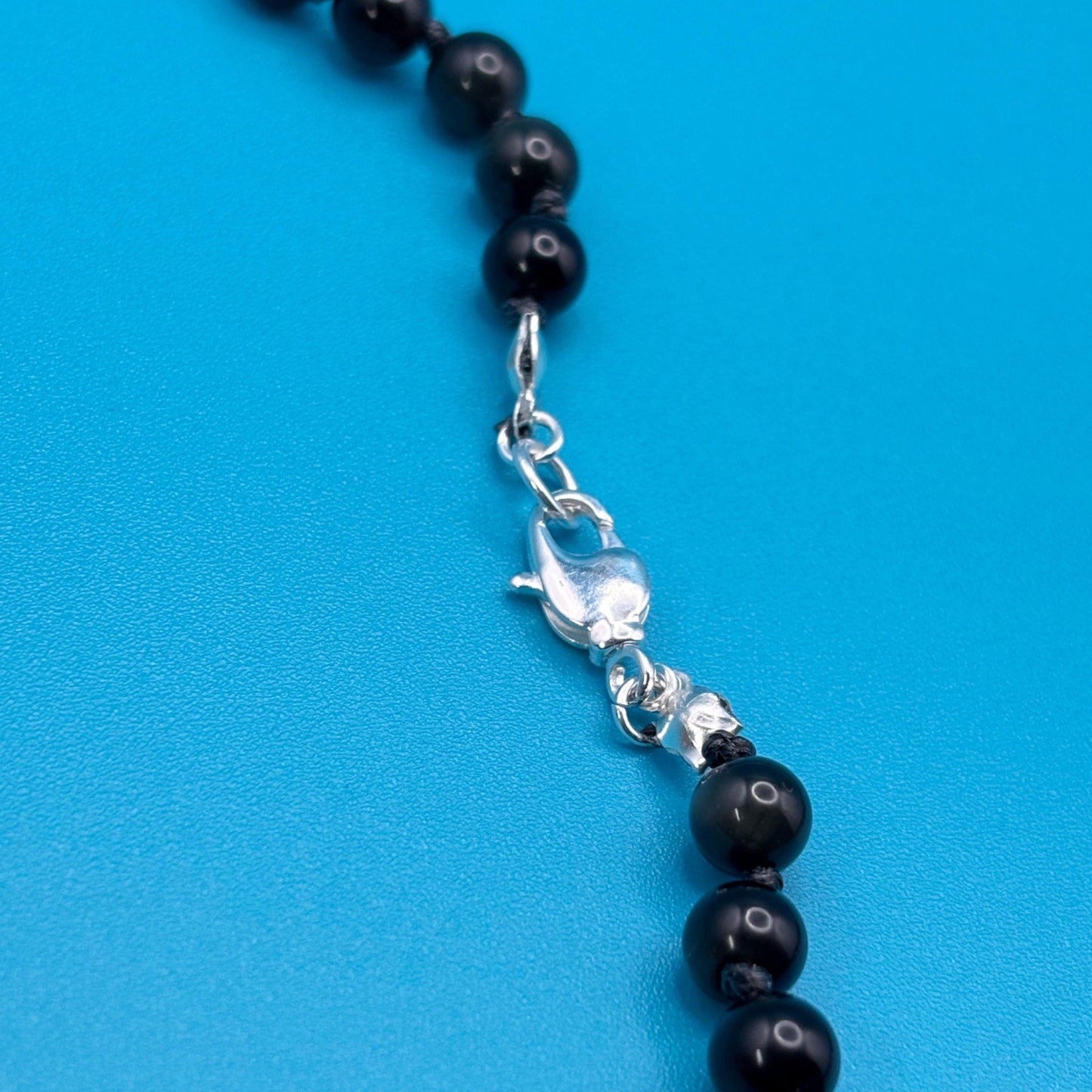 Black beaded necklace with a silver clasp on a blue background