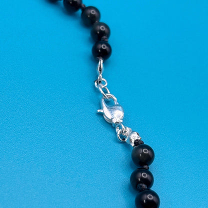 Black beaded necklace with a silver clasp on a blue background