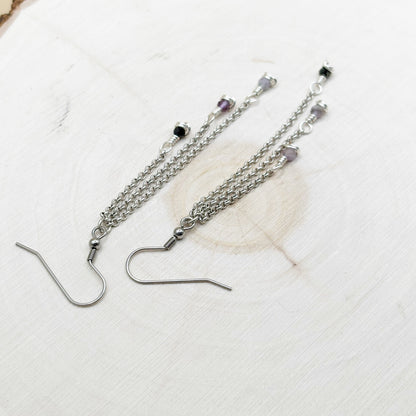 Silver chain earrings with gemstones on a textured white surface