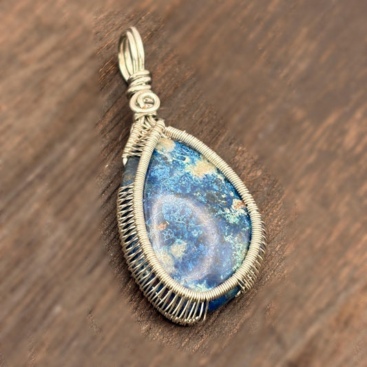Teardrop-shaped pendant with blue stone and wire wrapping on a wooden surface