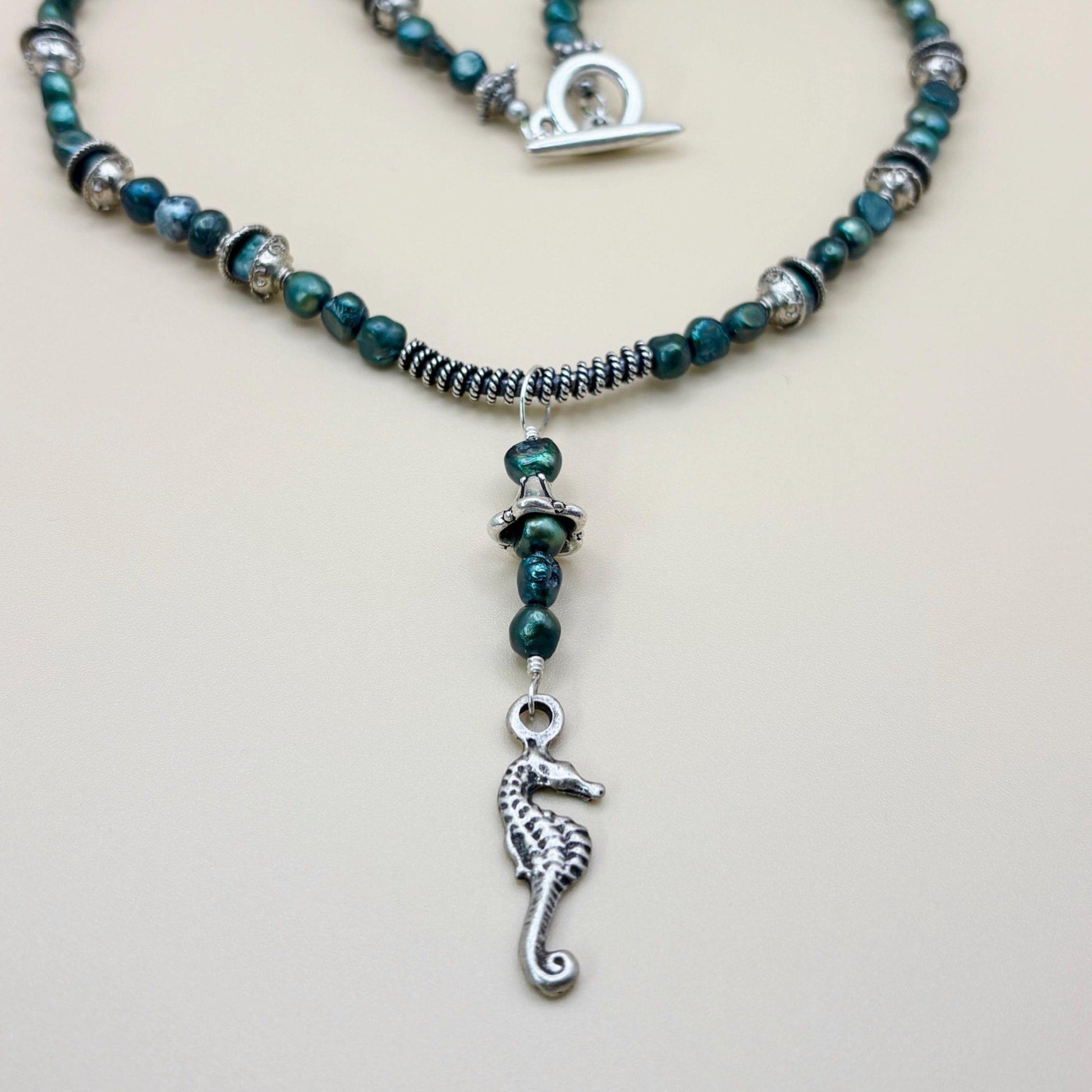 Necklace with green beads and a silver seahorse charm on a light gray background