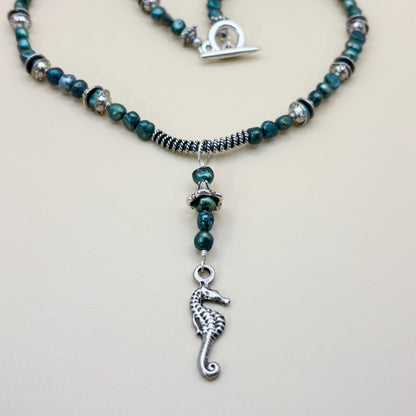 Necklace with green beads and a silver seahorse charm on a light gray background