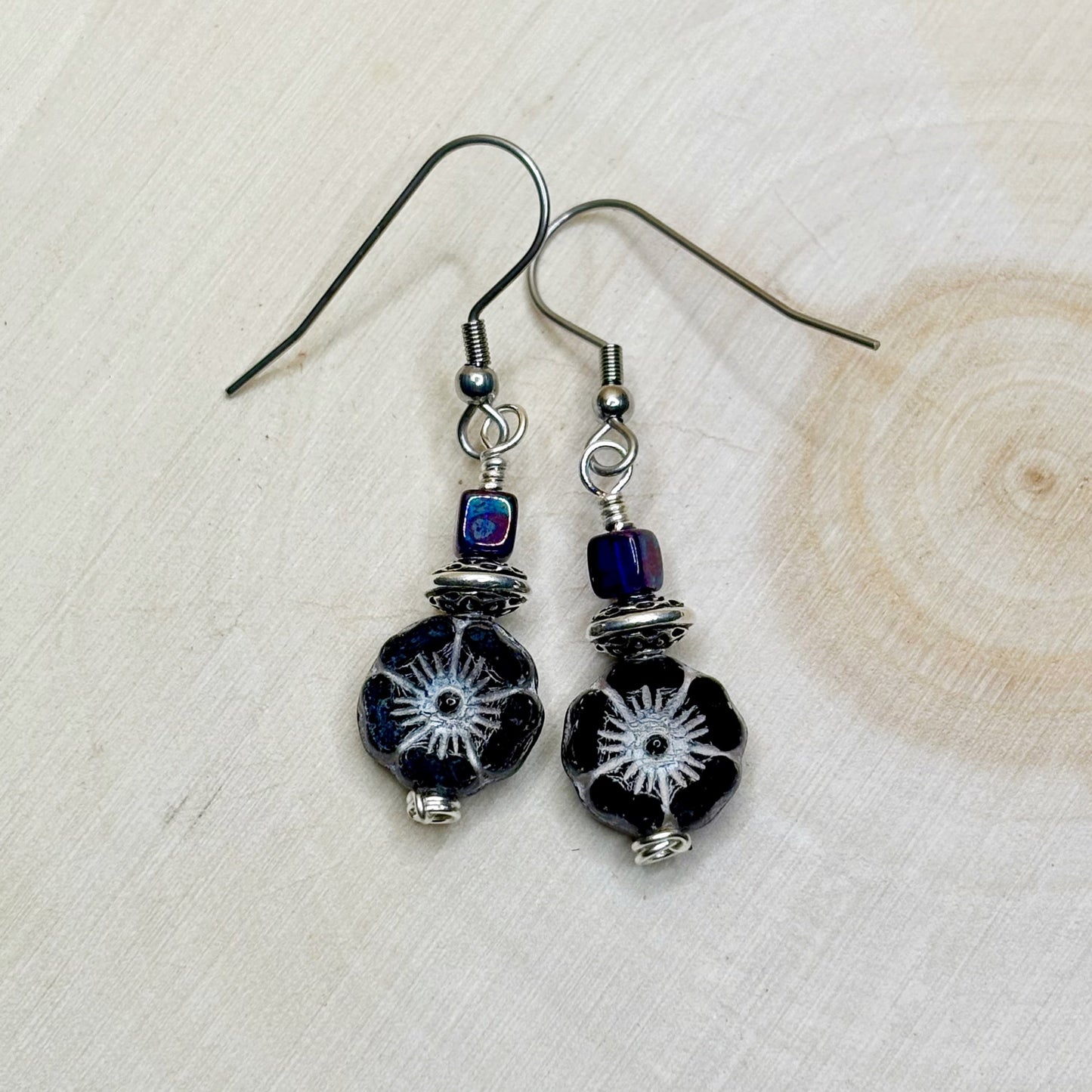 Pair of black beaded earrings with silver and blue accents on a light wooden surface.