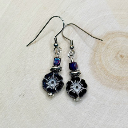 Pair of black beaded earrings with silver and blue accents on a light wooden surface.