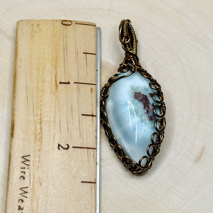 Pendant with blue stone and bronze wirework on a wooden ruler