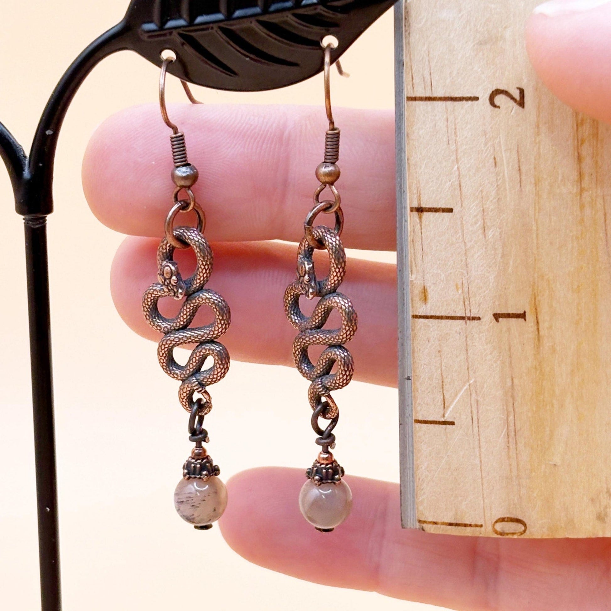 Pair of snake-style earrings held against a wooden ruler for size reference.