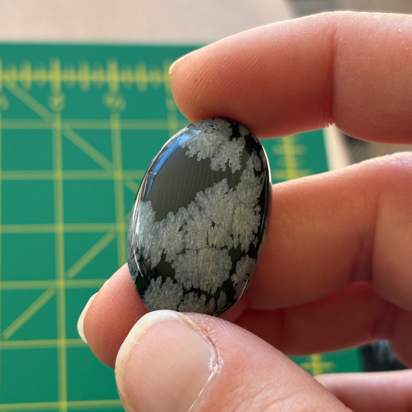 Hand holding a snowflake obsidian stone with a green cutting mat in the background