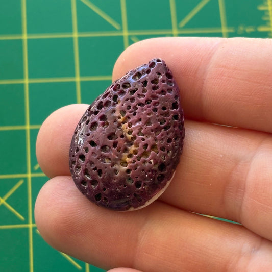 Hand holding a purple textured stone against a green cutting mat background-p
