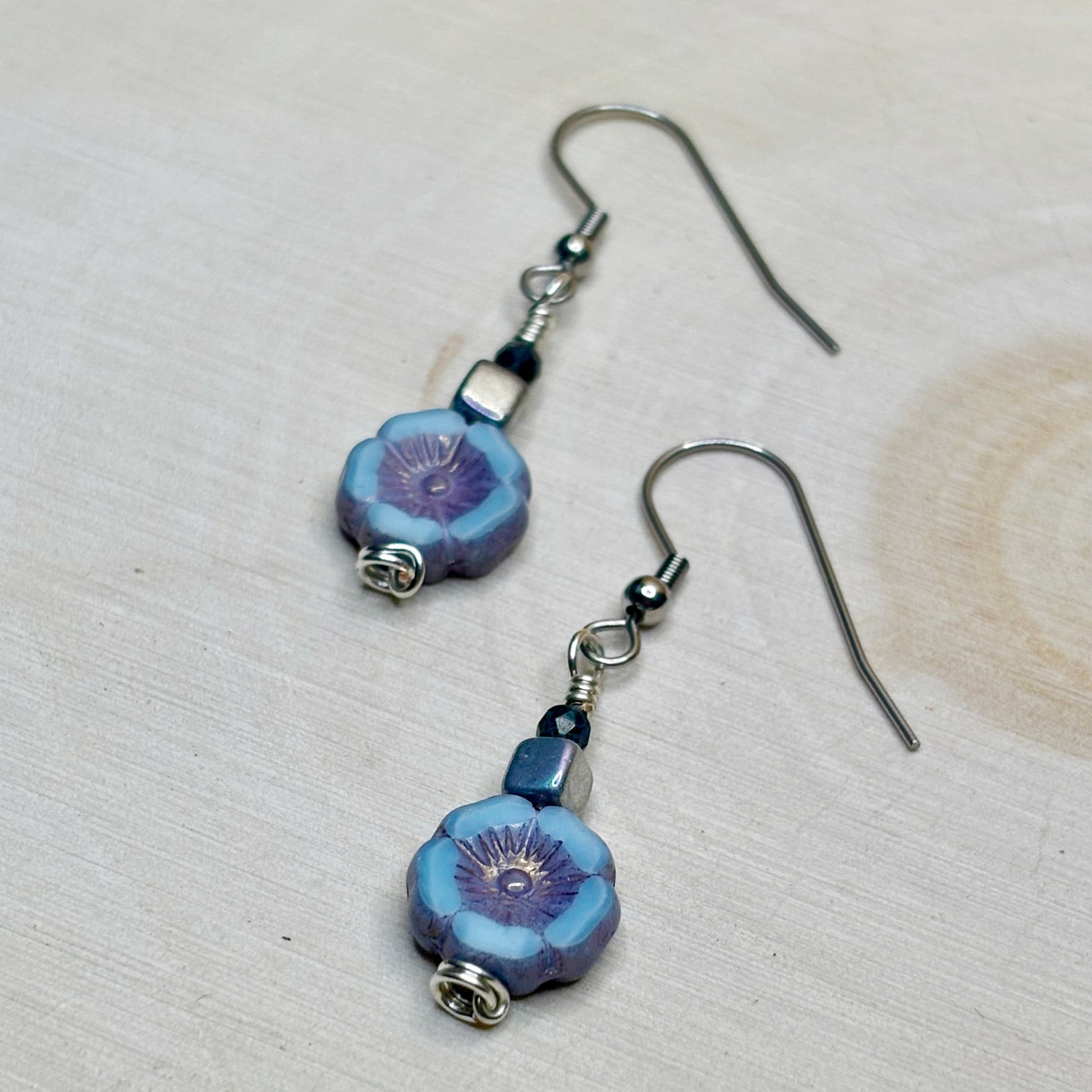 Pair of flower-shaped blue and purple beaded earrings on a light background