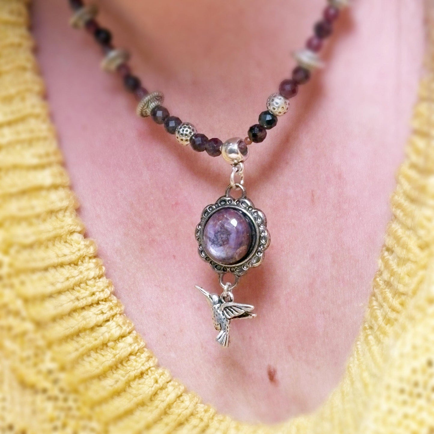 Necklace with a purple pendant and bird charm worn by a person in a yellow top.