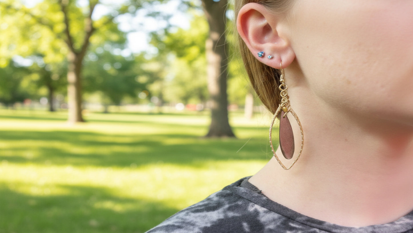 Close-up of a person wearing a pink teardrop earring with gold accents.