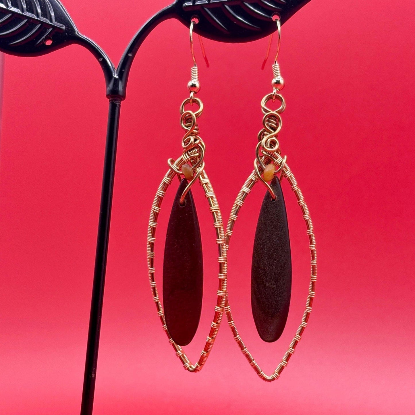 Gold-framed earrings with dark brown oval stones on a red background