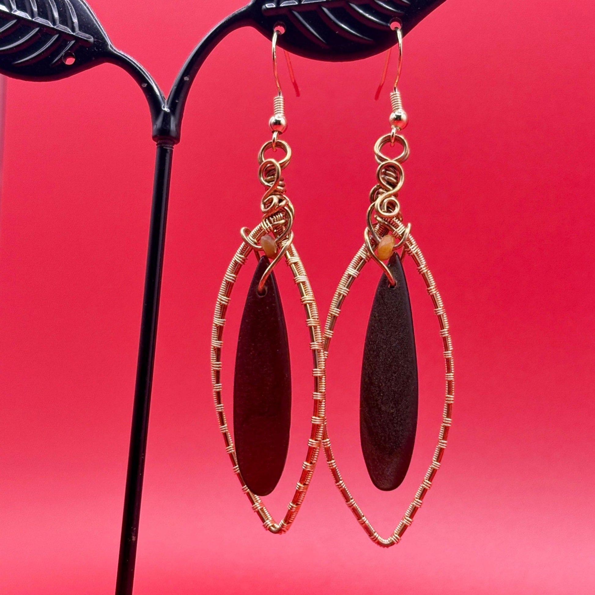 Gold-framed earrings with dark brown oval stones on a red background