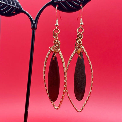 Gold-framed earrings with dark brown oval stones on a red background