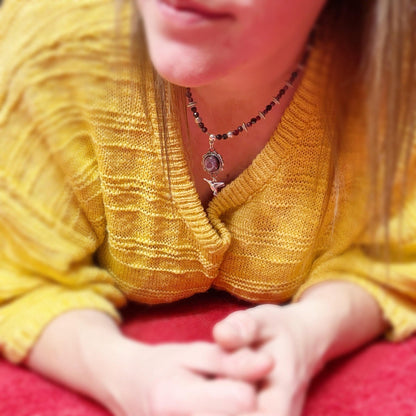 Person wearing a yellow sweater with a necklace, sitting on a red surface.