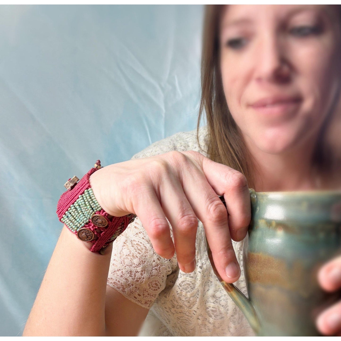 Woman holding a mug with a decorative wristband on her wrist.