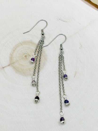 Silver chain earrings with purple beads on a light wood background