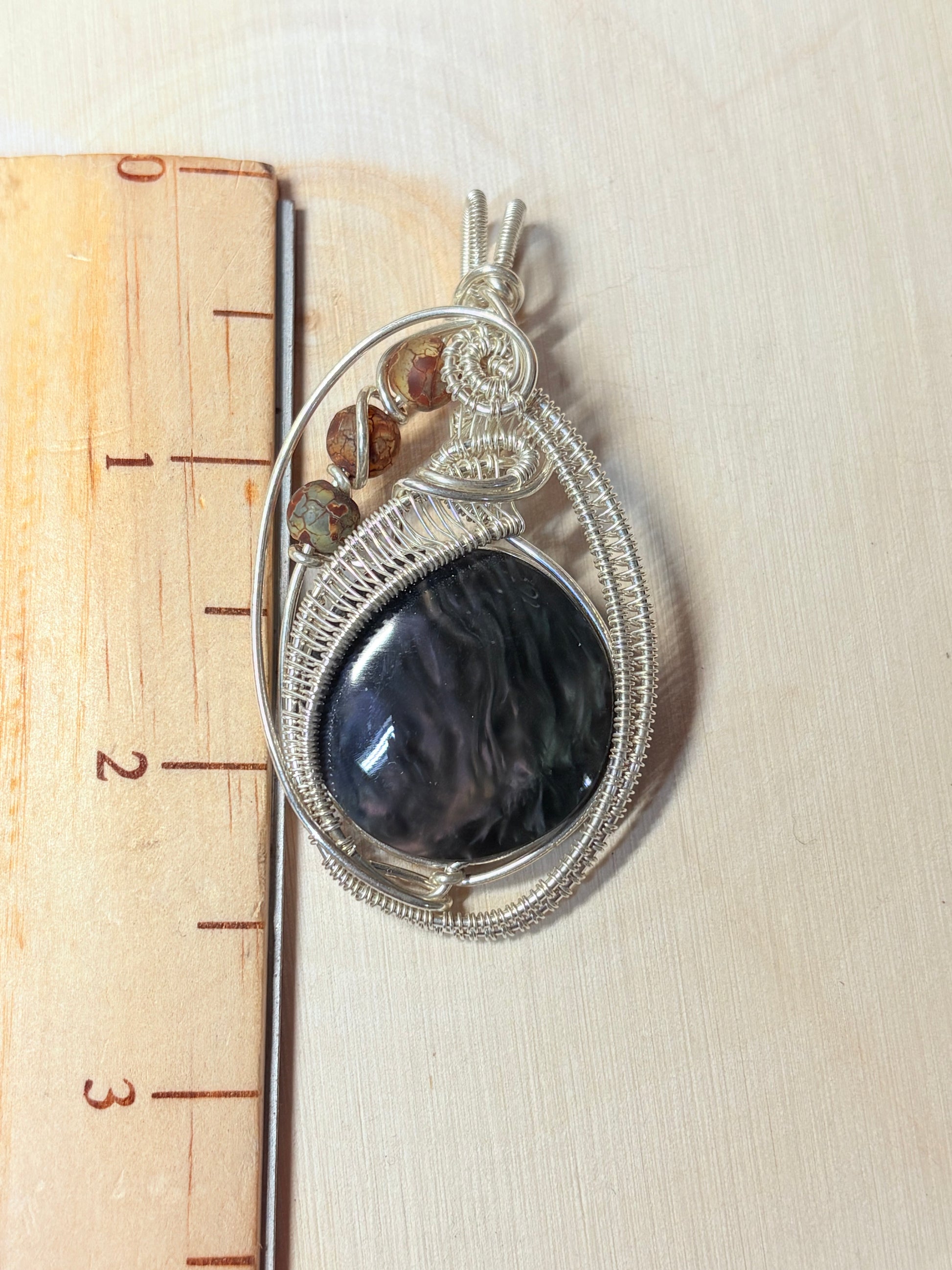 Silver pendant with a dark stone on a wooden ruler