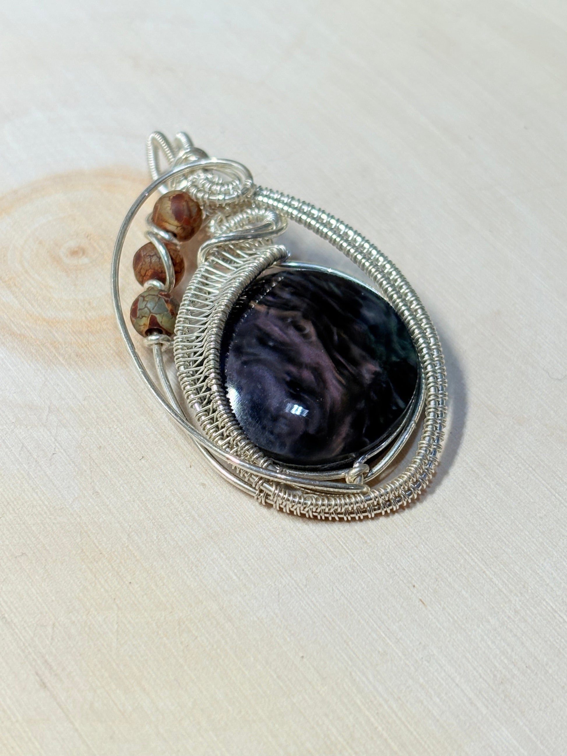 Silver pendant with a purple stone on a beige wood background