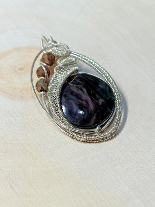 Silver pendant with a purple stone on a beige wood background
