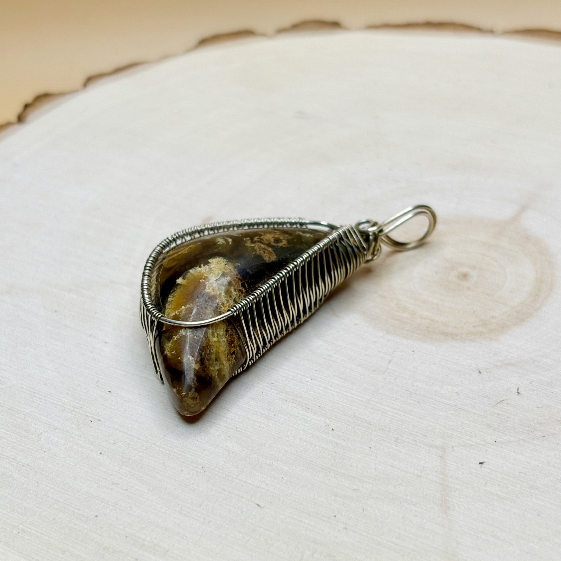 Crescent moon shaped amber wire wrapped in sterling silver necklace pendant sitting on a wooden background 