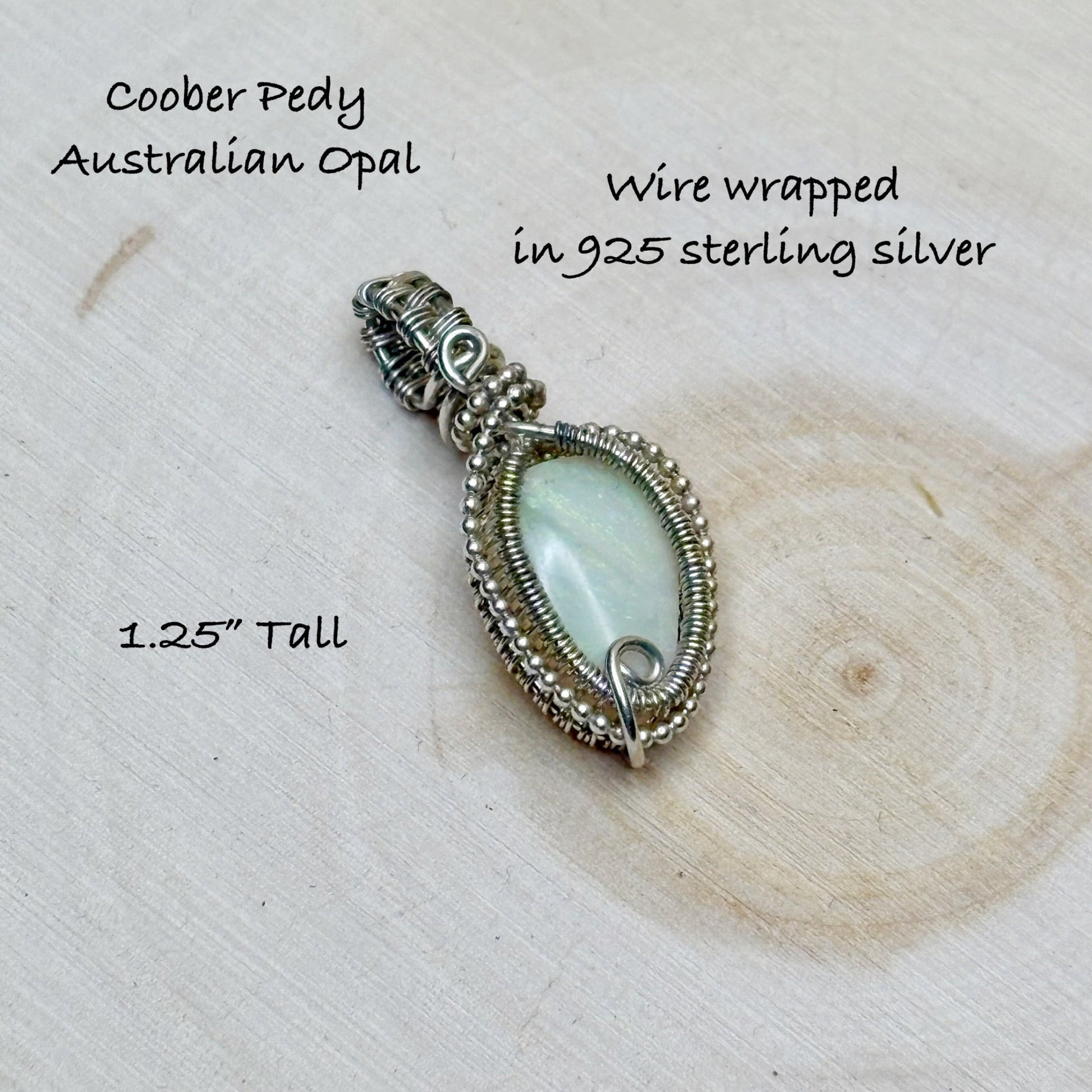 Silver wire-wrapped pendant with opal stone on a wooden surface