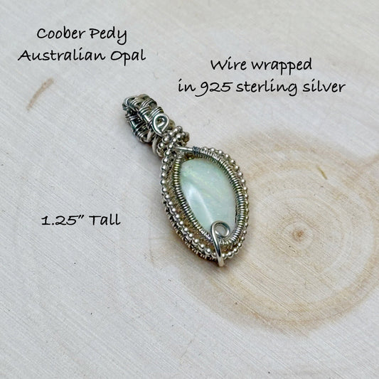 Silver wire-wrapped pendant with opal stone on a wooden surface