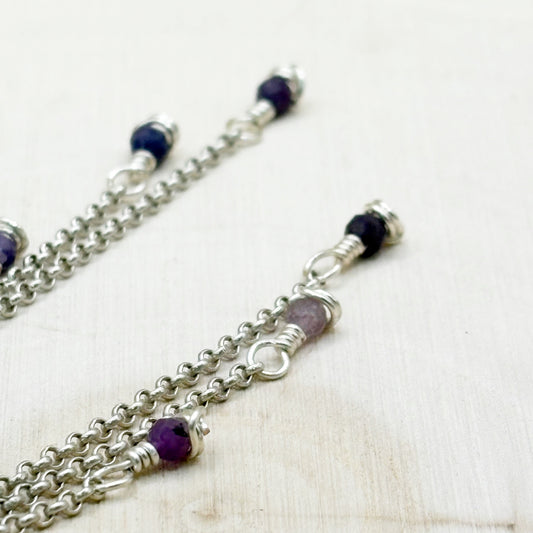 Silver chain bracelet with purple beads on a white background