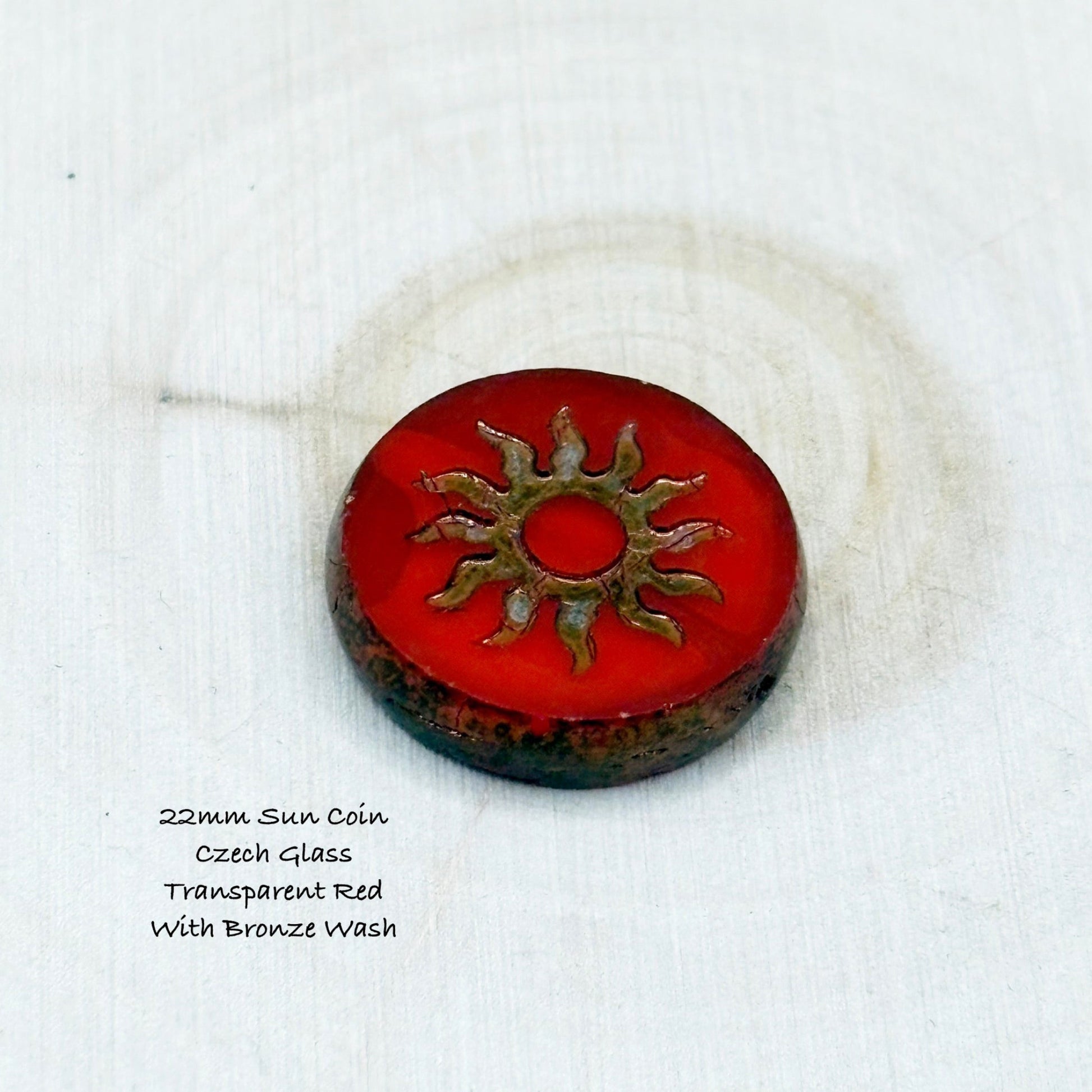 Red coin-shaped object with bronze sun design on a white background