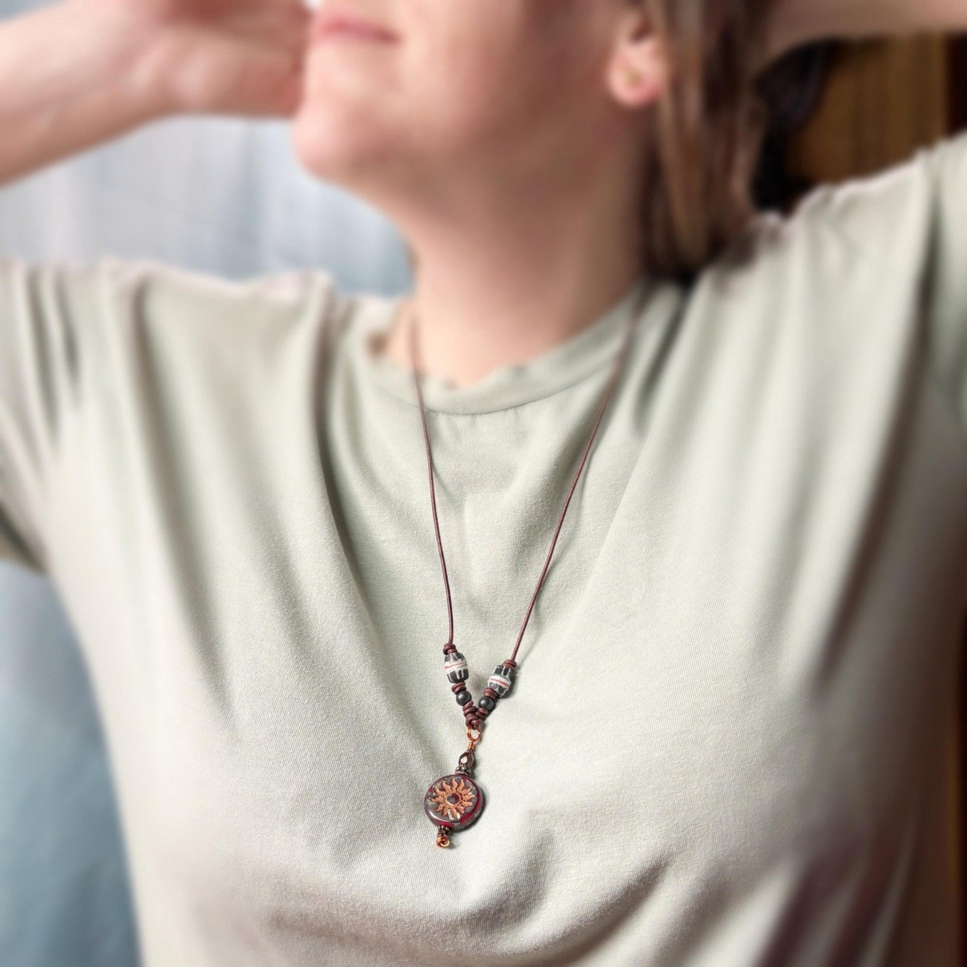 Person wearing a light-colored shirt with a beaded necklace featuring a circular pendant.